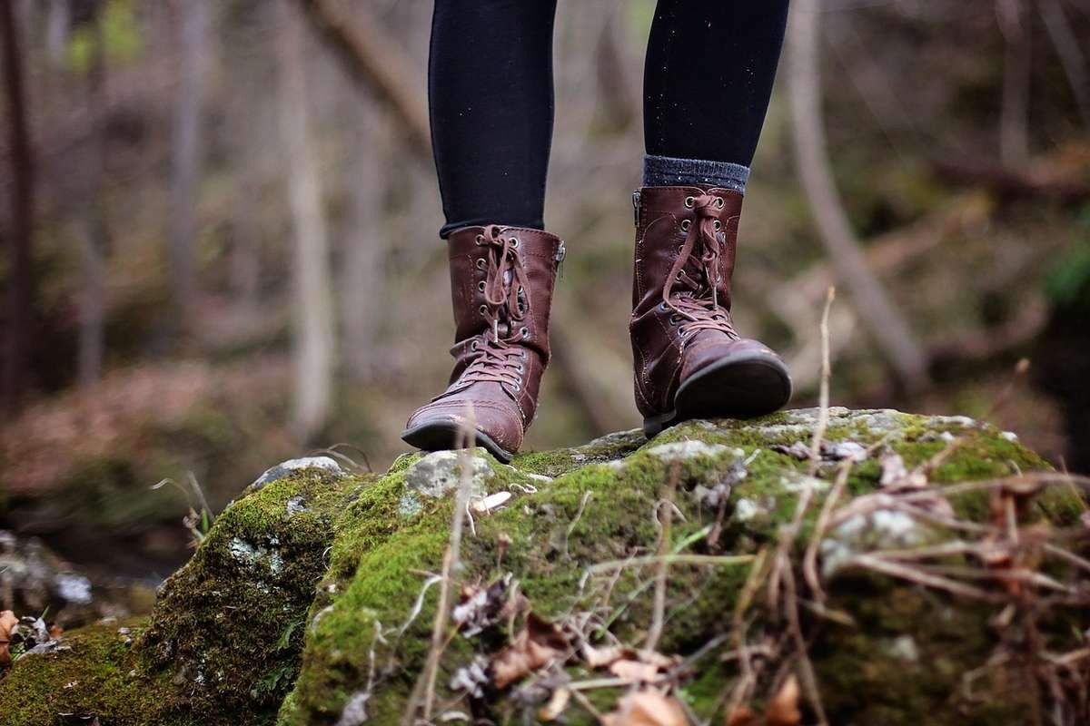 Pieds chaussés de bottes de randonnée sur un tronc recouvert de mousse en forêt