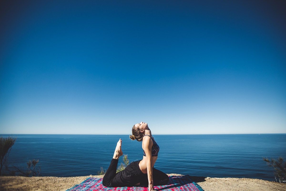 Femme en posture de yoga sur tapis, au bord de la mer, ciel bleu