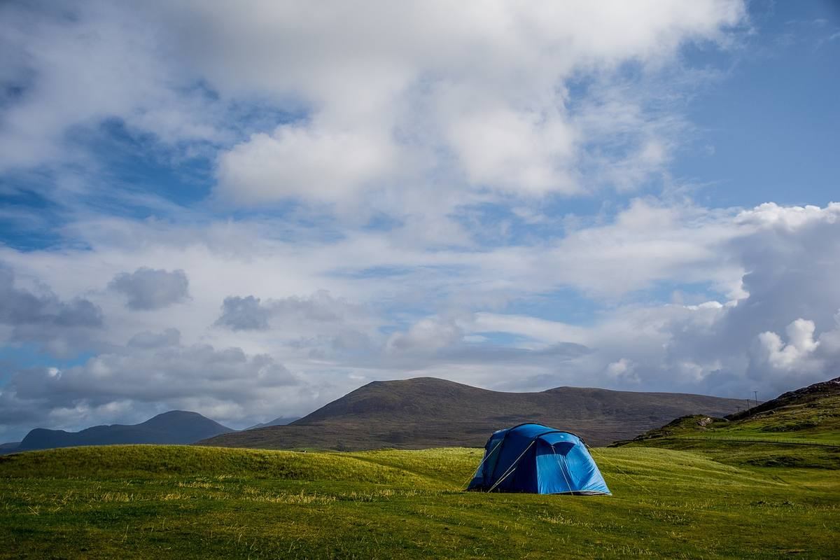 Un tente bleue solitaire sur prairie verdoyante, montagnes lointaines, ciel nuageux Un tente bleue solitaire sur prairie verdoyante, montagnes lointaines, ciel nuageux
