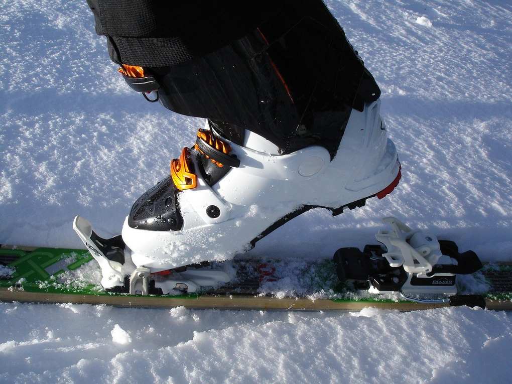 Botte de ski blanche et noire fixée sur une planche, sur fond de neige