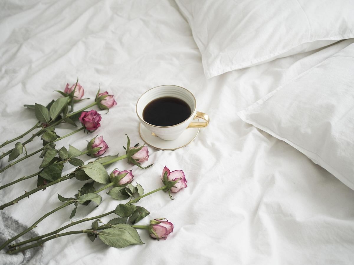 Tasse de café sur lit avec roses fanées et oreillers blancs