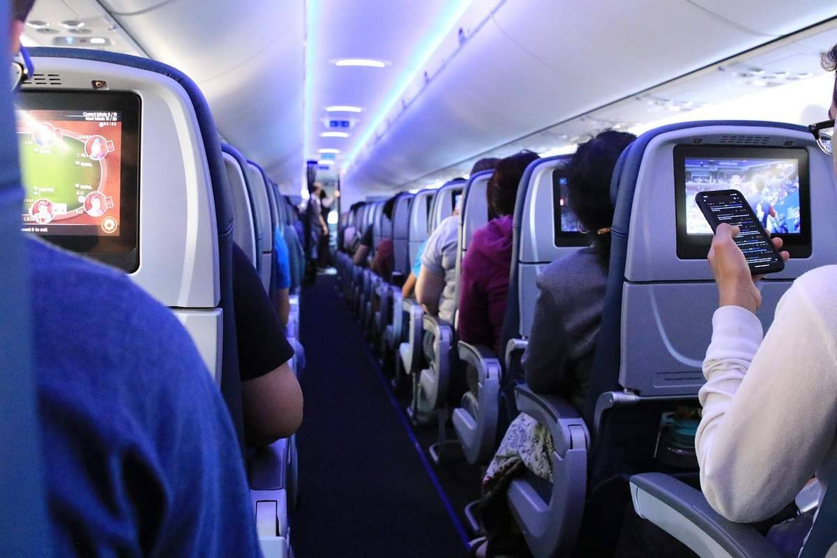 Passagers dans un avion, écrans de divertissement et téléphone visible